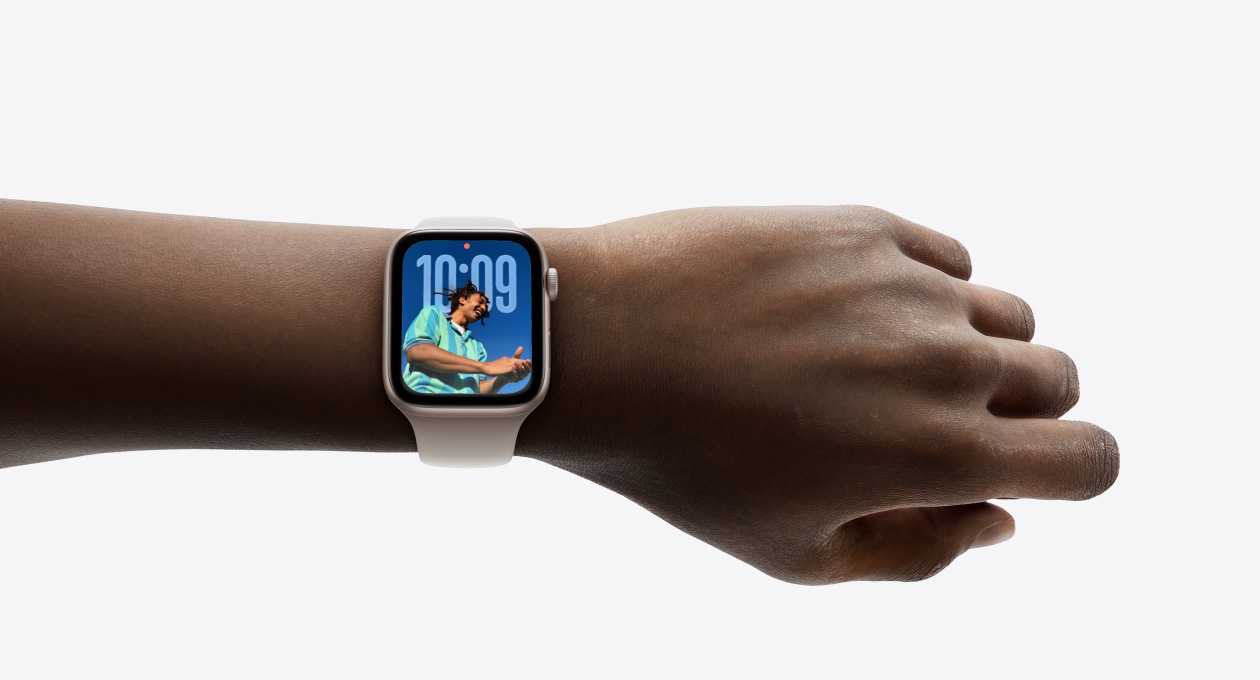 Vue rapprochée d’une Apple Watch argent assortie d’un bracelet en caoutchouc sur un poignet; on y voit l’heure dans le nouveau design avec Liquid Glass