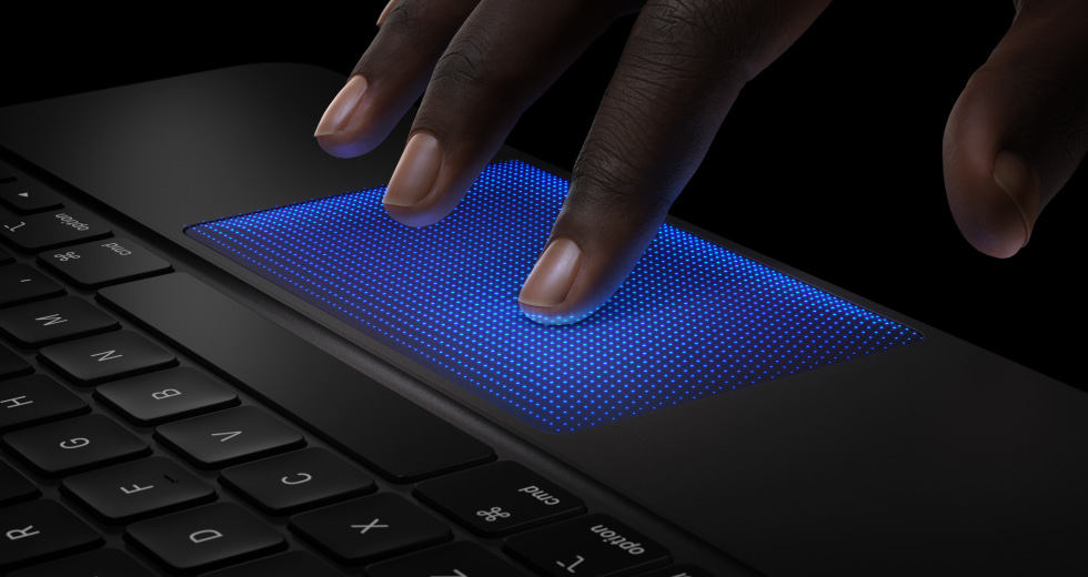 Animation d’une main avec doigts survolant le trackpad du Magic Keyboard, index avec ombre bleue montrant l’action de toucher pour illustrer le retour haptique